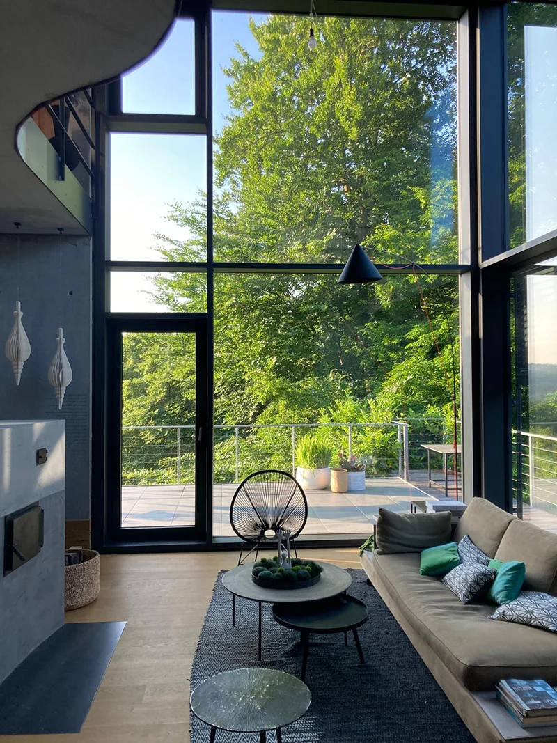 Lichtdurchfluteter Wohnbereich mit doppelter Raumhöhe, raumhoher Glasfassade, offener Architektur und Blick auf Terrasse und Natur – moderne Wohnhausplanung eines Architekturbüros.