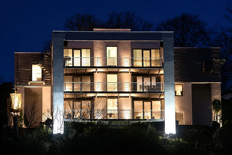 Modernes Mehrfamilienhaus mit großzügigen Balkonen und architektonischem Lichtkonzept bei Nacht – Planung und Umsetzung im Wohnungsbau.
